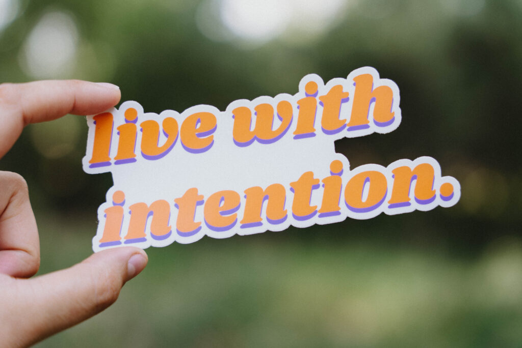Sticker that says "live with intention" held up in front of a green background